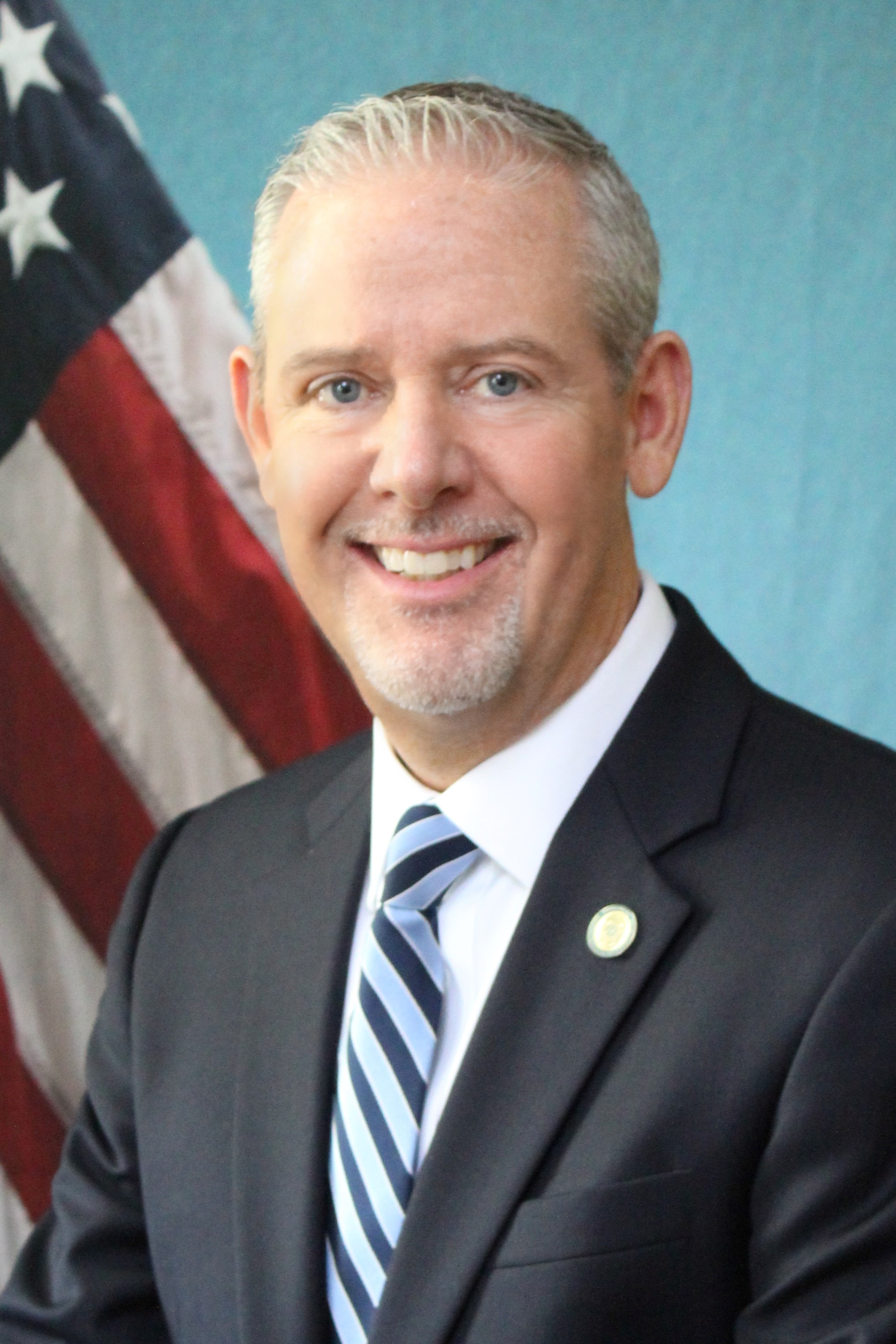 Portrait photo of smiling white man in front of the American flag.