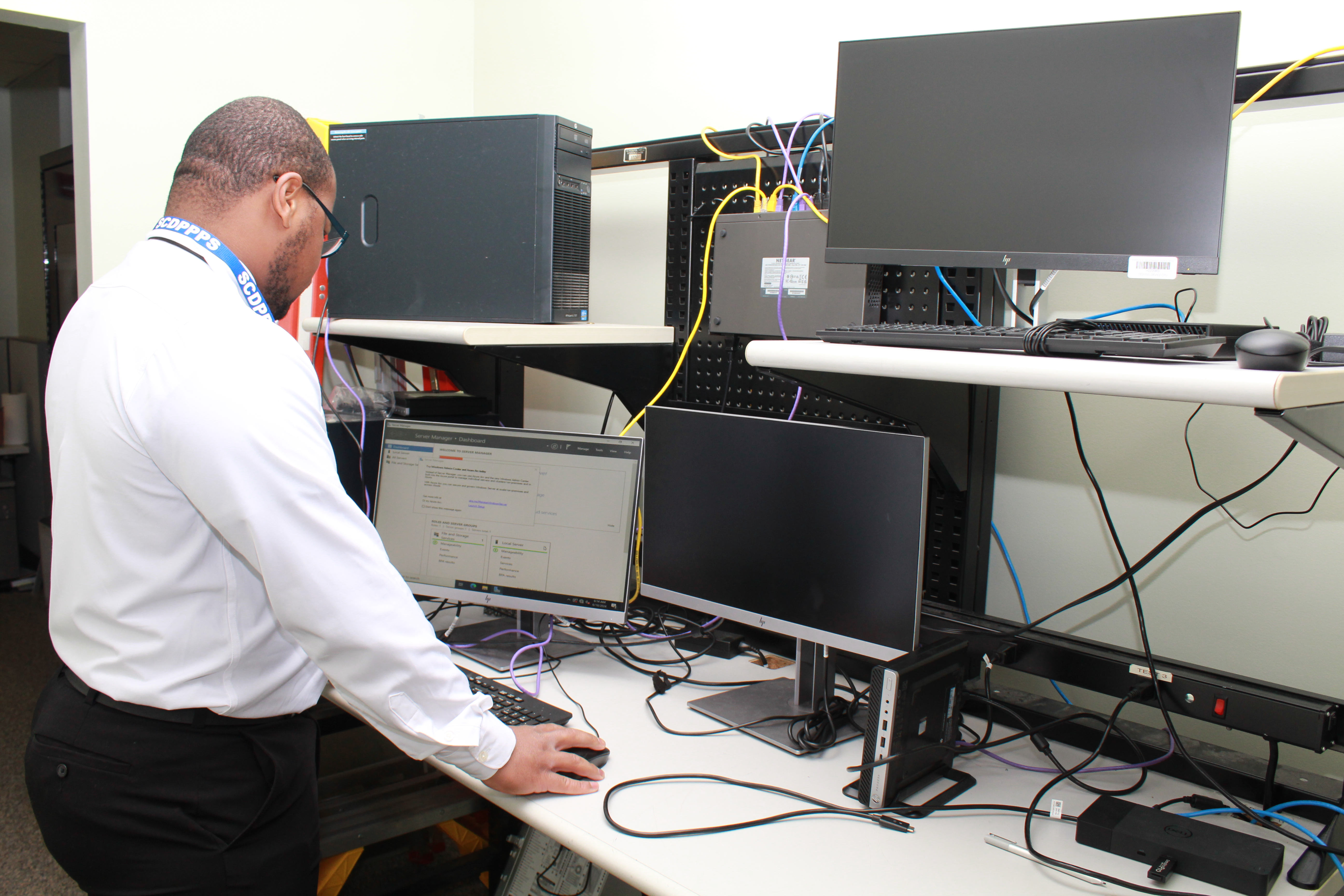 Man standing at a desk with computer equipment.