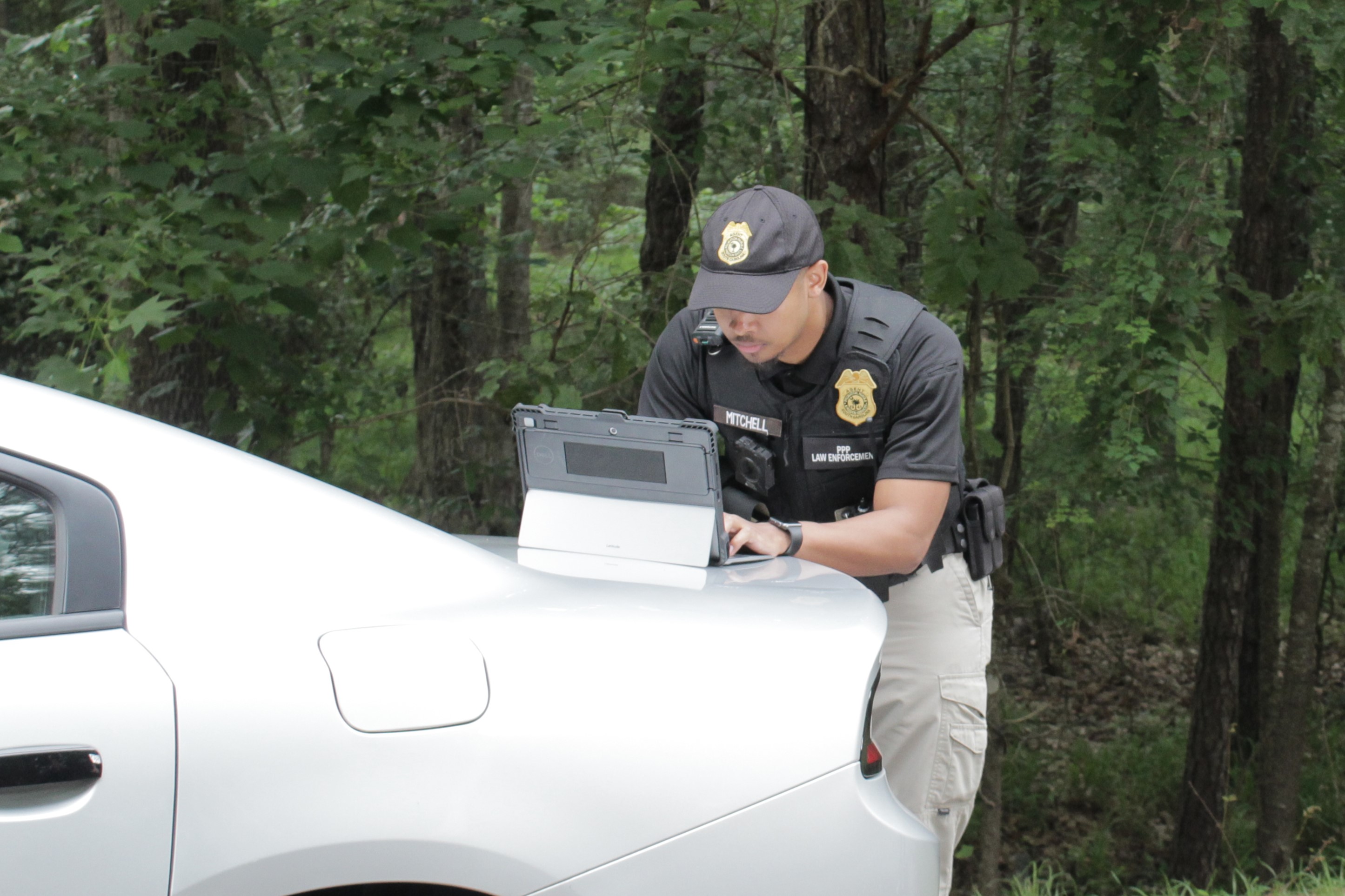 An agent is hunched over, typing on a laptop placed on the closed trunk of a car.