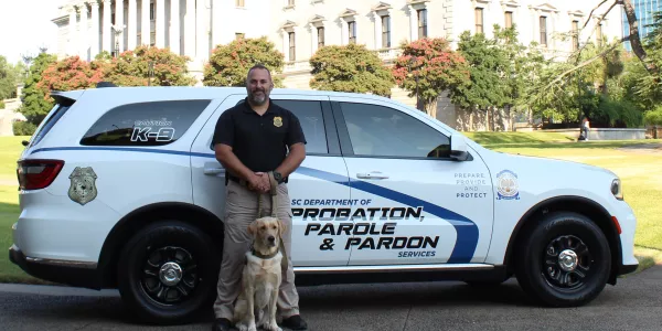 Agent Benjy and K-9 Chip standing in beside the SCDPPPS vehicle.